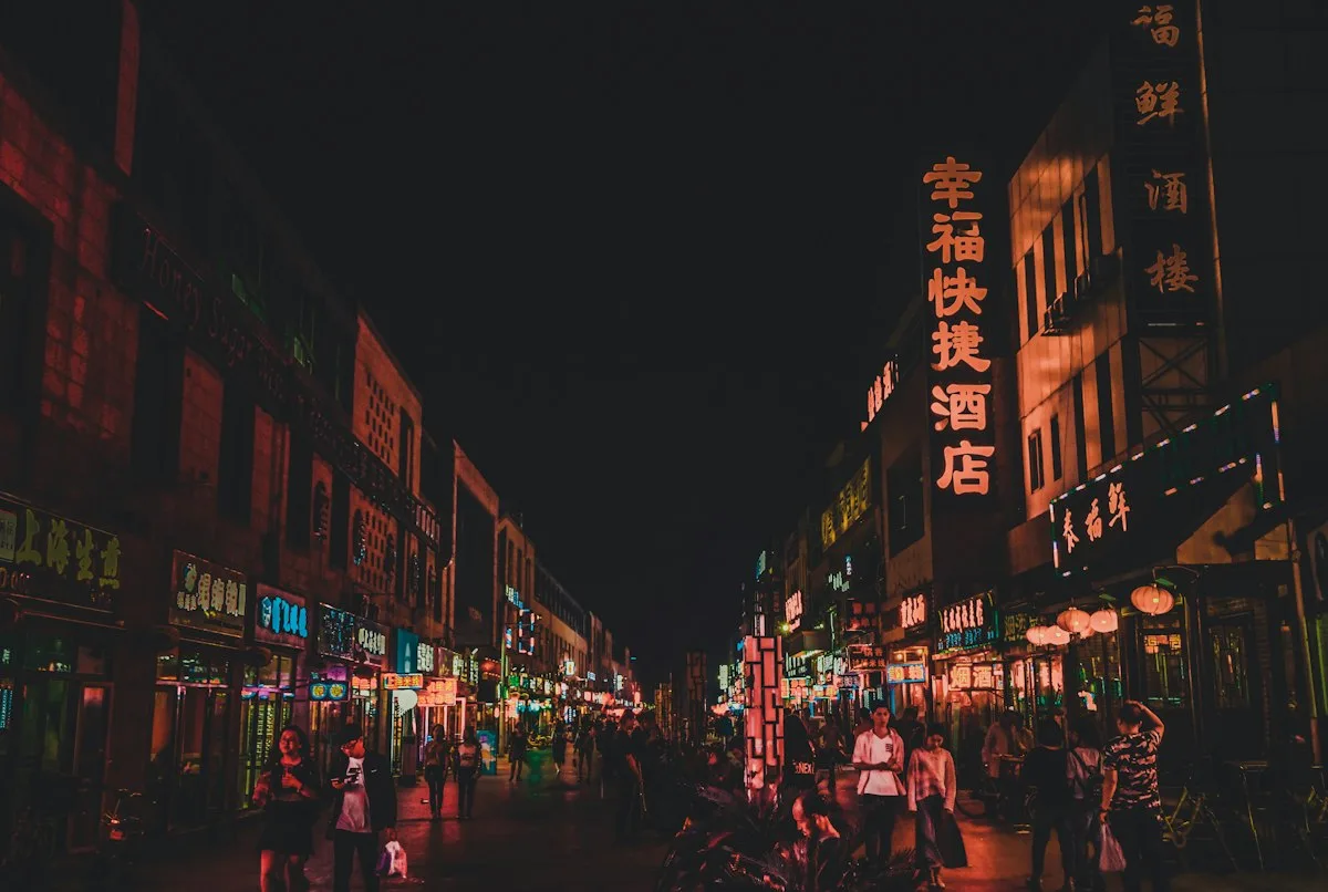 A busy Chinese commercial street at night, lit by shop signs in Chinese