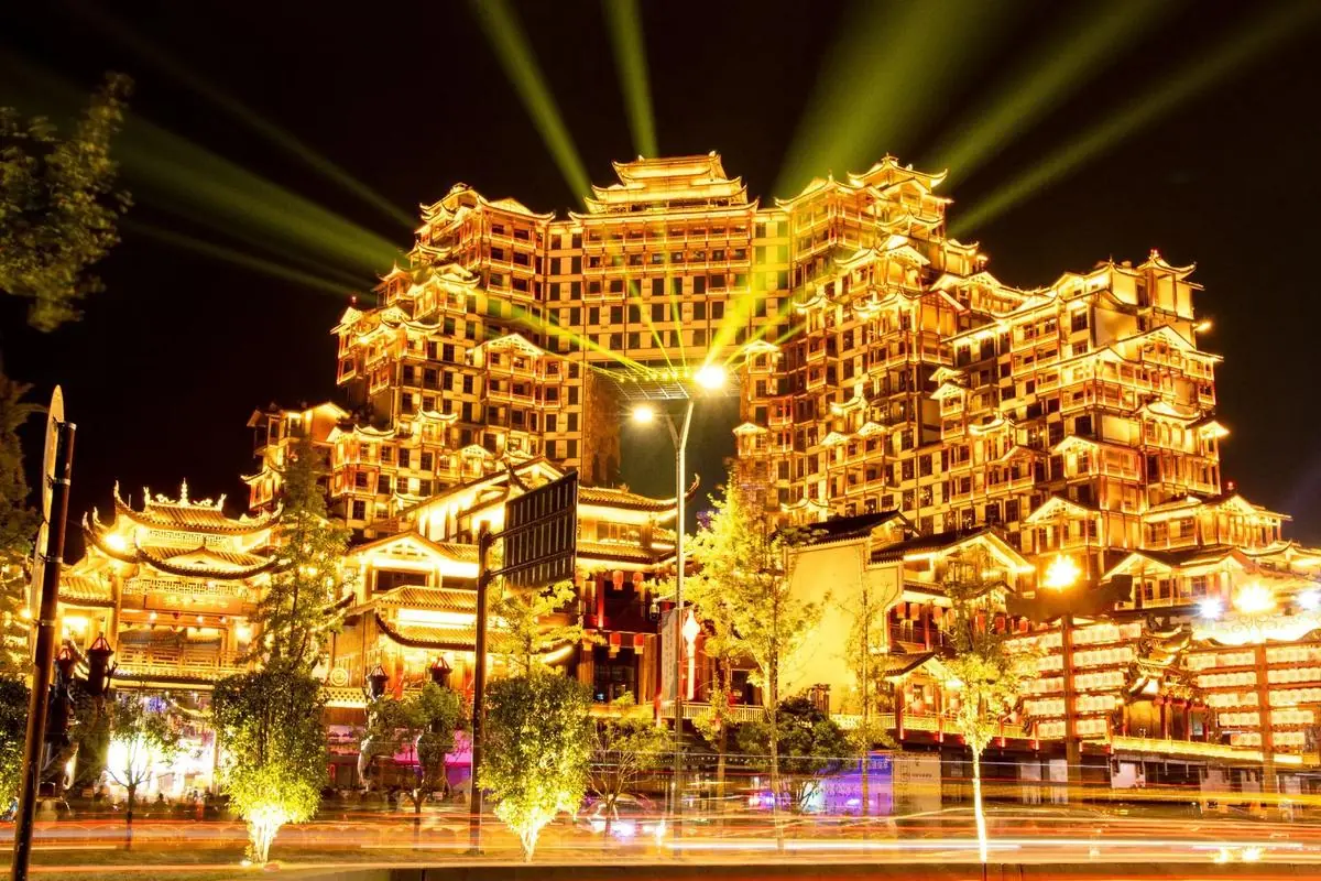 The 72 Qilou stilted-building complex lit up at night, green spotlights sweeping the sky above its stacked tiled roofs