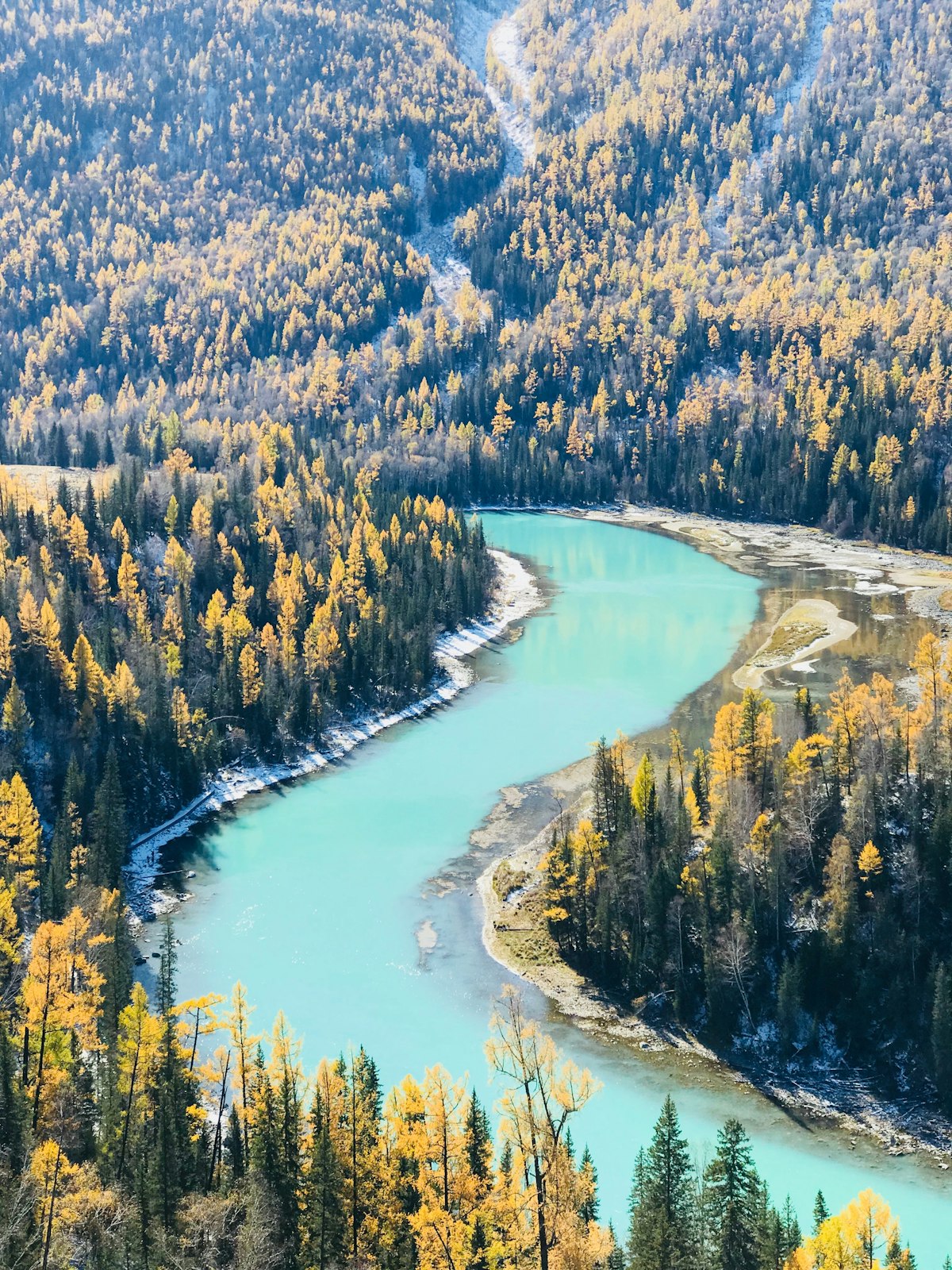Aerial view of Kanas Lake in Xinjiang — turquoise water surrounded by dense forest and snow-dusted mountains