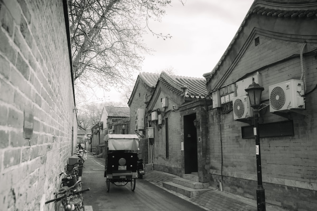 A narrow Beijing hutong side alley — grey brick walls, rickshaws, and the quiet rhythm of old Beijing life away from the tourist crowds