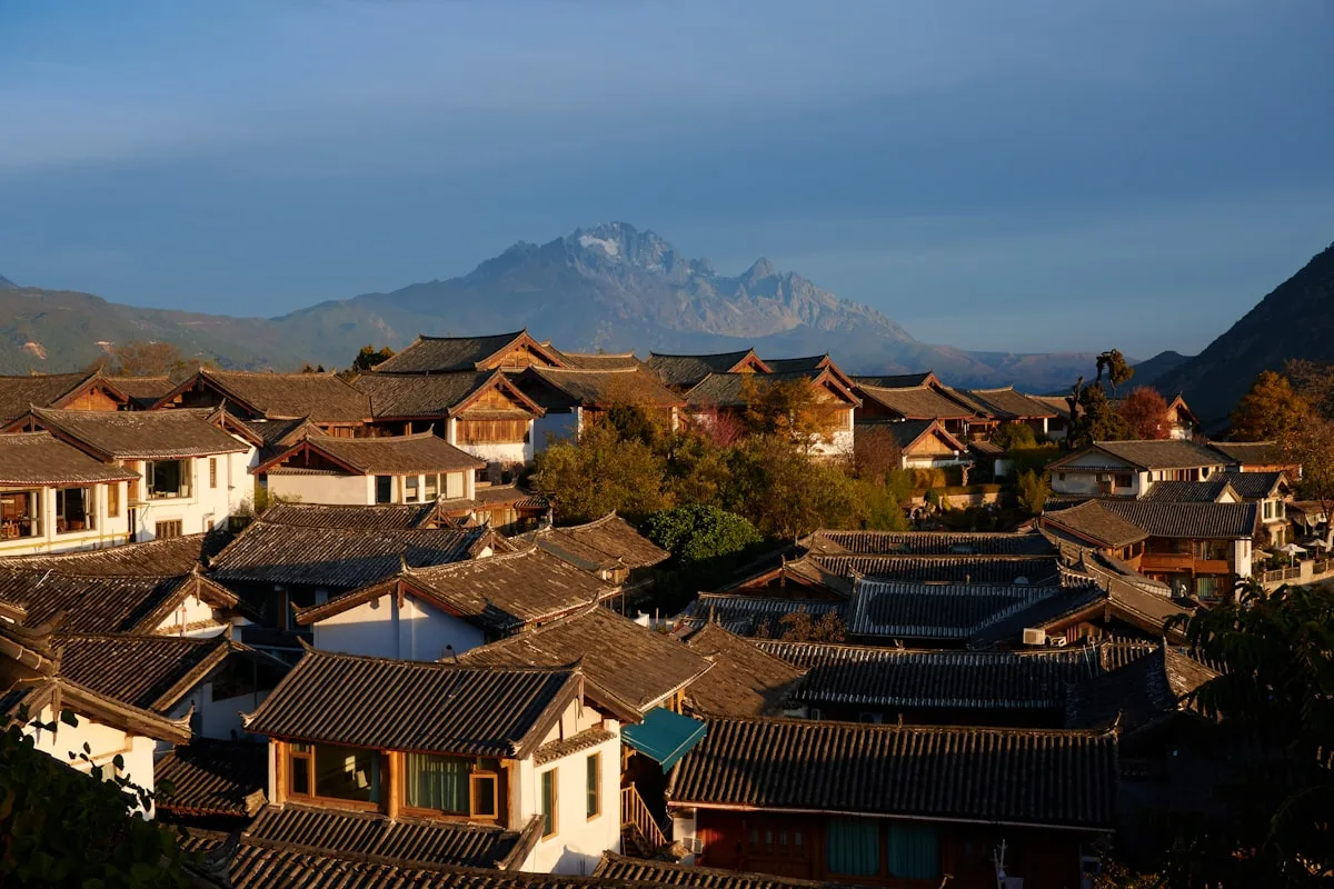 Techos tradicionales de aldea con montañas de fondo al amanecer en Lijiang, Yunnan