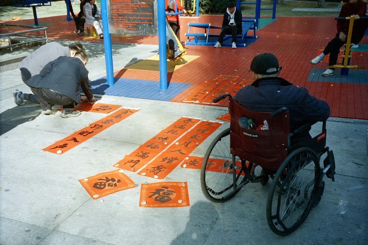 Man in wheelchair watches people arrange calligraphy scrolls.