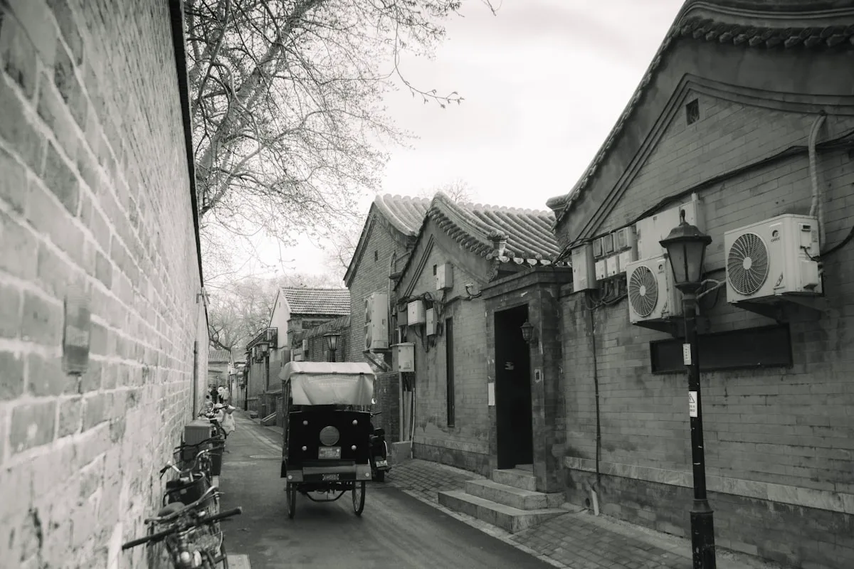 A narrow Beijing hutong side alley — grey brick walls, rickshaws, and the quiet rhythm of old Beijing life away from the tourist crowds