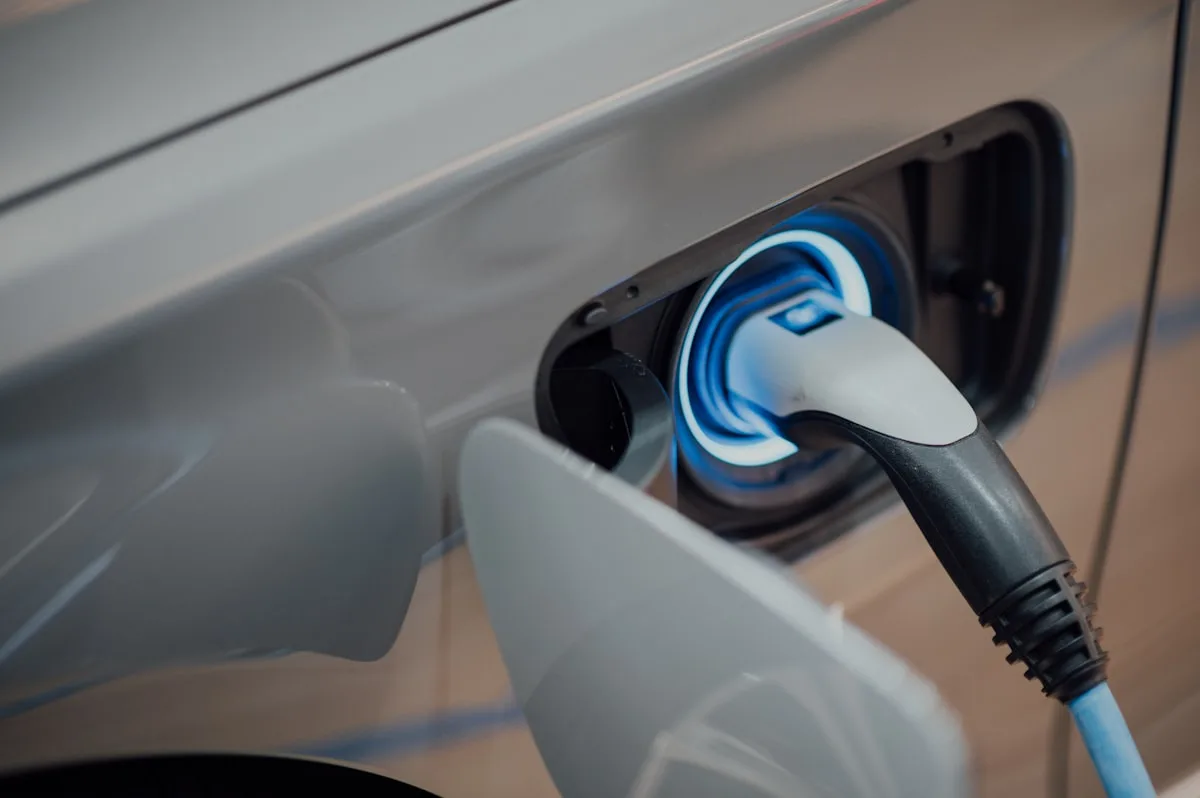 Un coche eléctrico plateado cargando, con el cable conectado al puerto y una luz azul