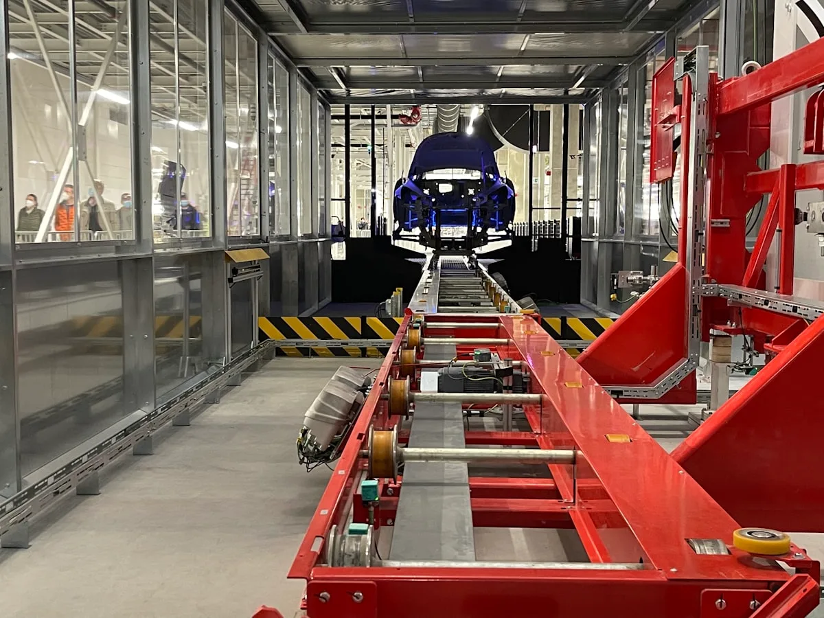 Una línea de montaje de una fábrica china de coches eléctricos vista desde una galería acristalada para visitantes, con carrocerías avanzando por la cinta