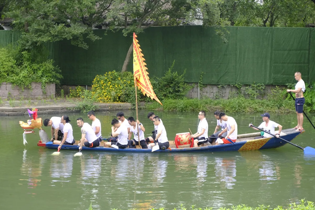 Des rameurs en chemise blanche pagayant un bateau-dragon décoré le long d'un canal dans une ville d'eau chinoise