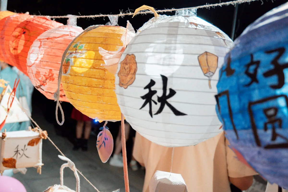 Des lanternes chinoises en papier illuminées, décorées de motifs peints, suspendues au-dessus d'une foule nocturne pendant la mi-automne