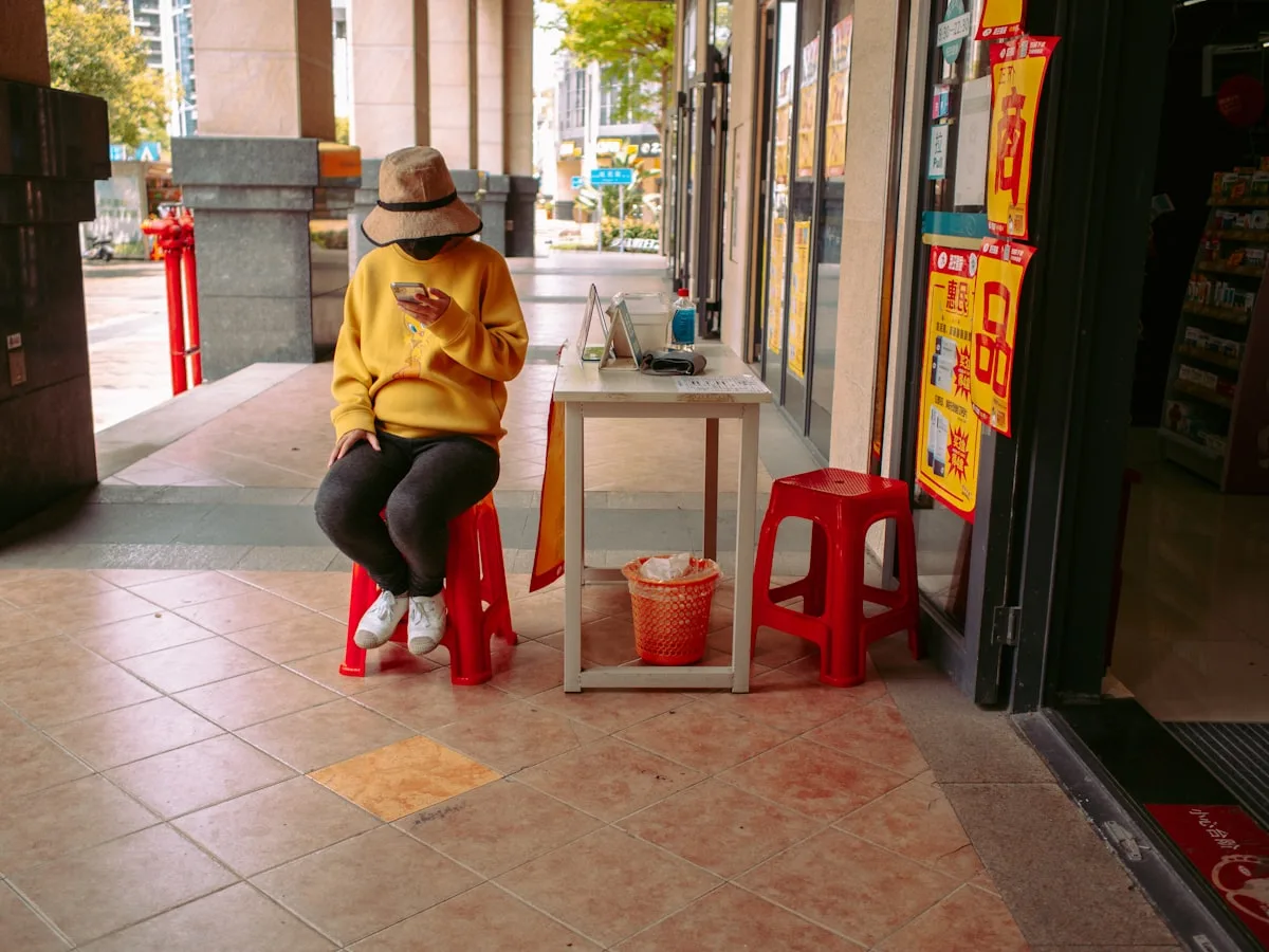 A person in a Chinese street checking their phone while seated at a small shop