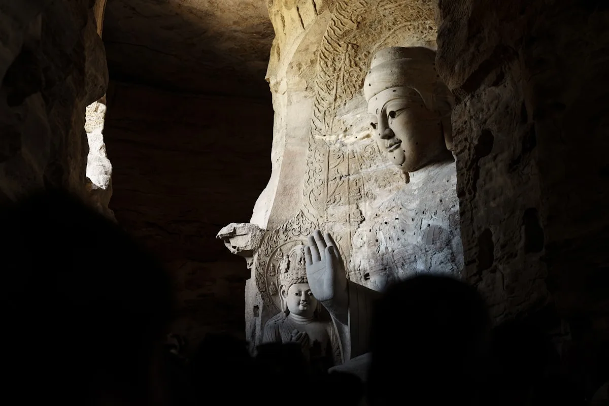 Large carved buddha statues inside a dark cave with visitors.