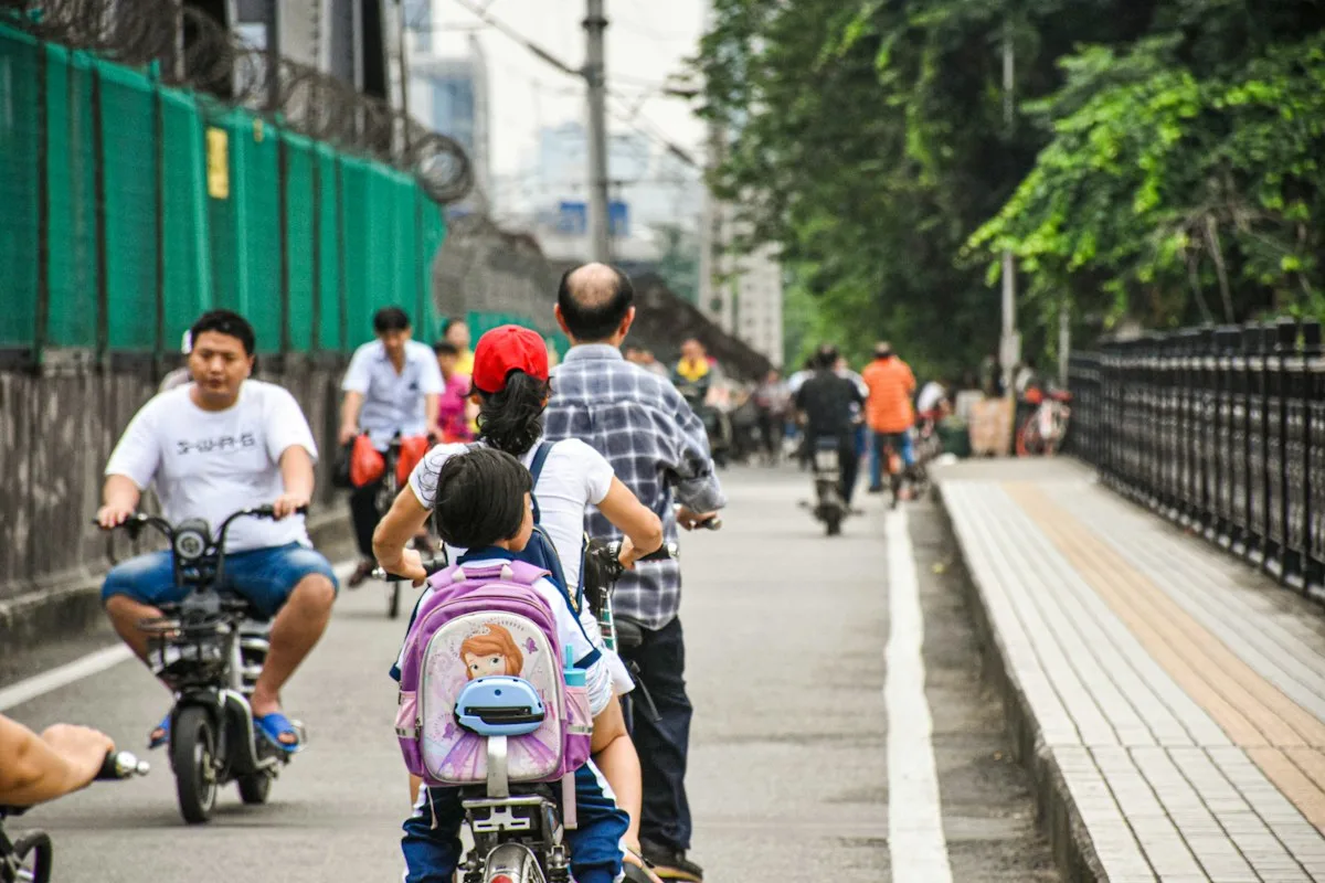 A parent riding an electric bike with a schoolchild on the back through Chinese city traffic
