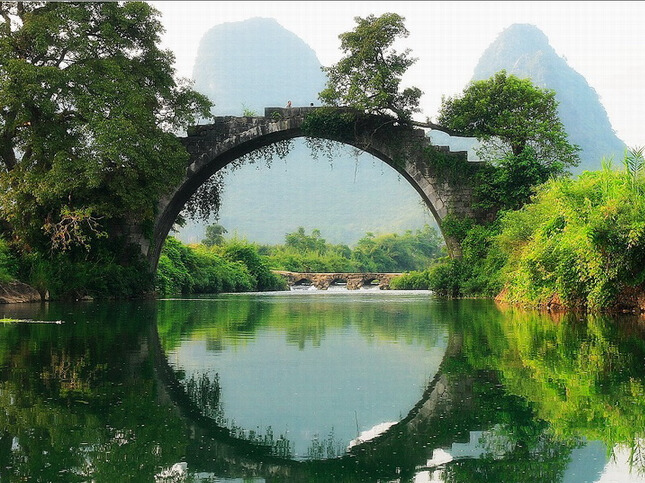 Fuli Bridge — a 500-year-old Ming Dynasty stone arch bridge forming a perfect circle with its reflection in the still Yulong River