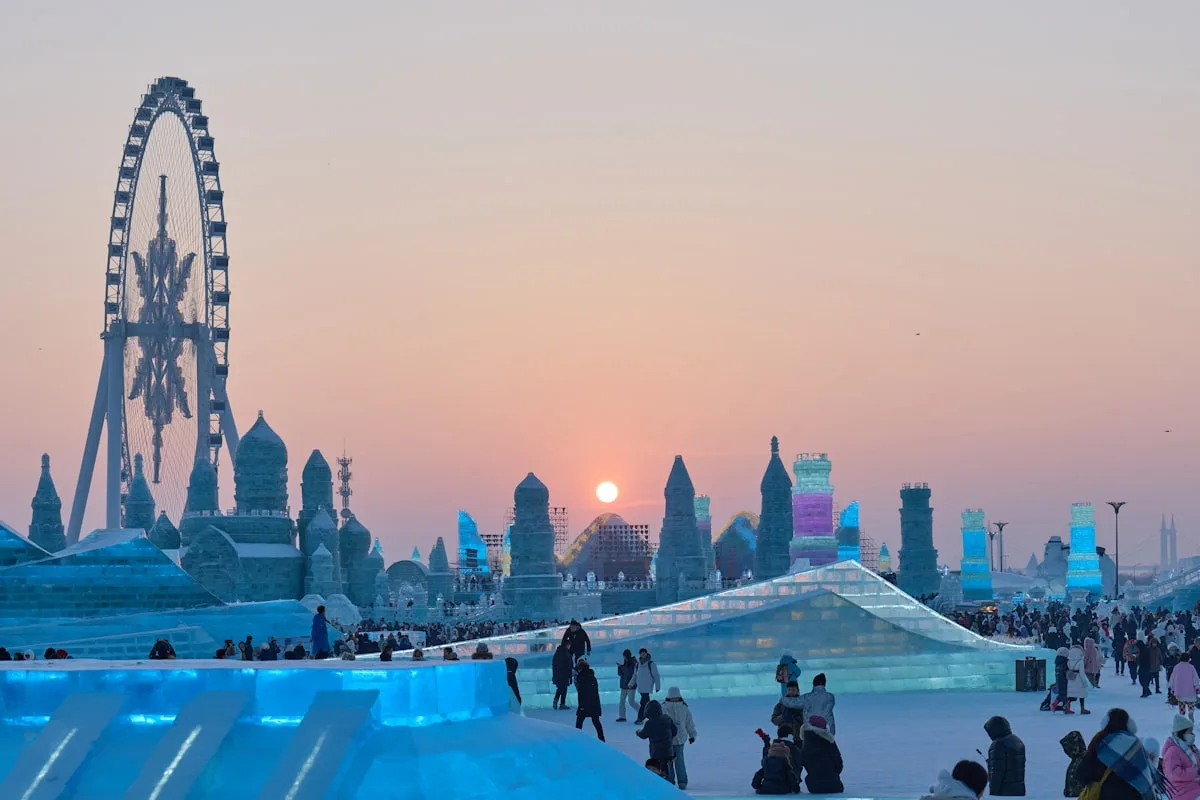 O Mundo de Gelo e Neve de Harbin ao pôr do sol, torres de gelo e uma grande roda-gigante sobressaindo sobre os caminhos nevados