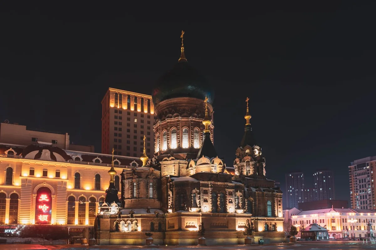 A catedral de Santa Sofia de Harbin iluminada por refletores à noite, cercada de chão coberto de neve