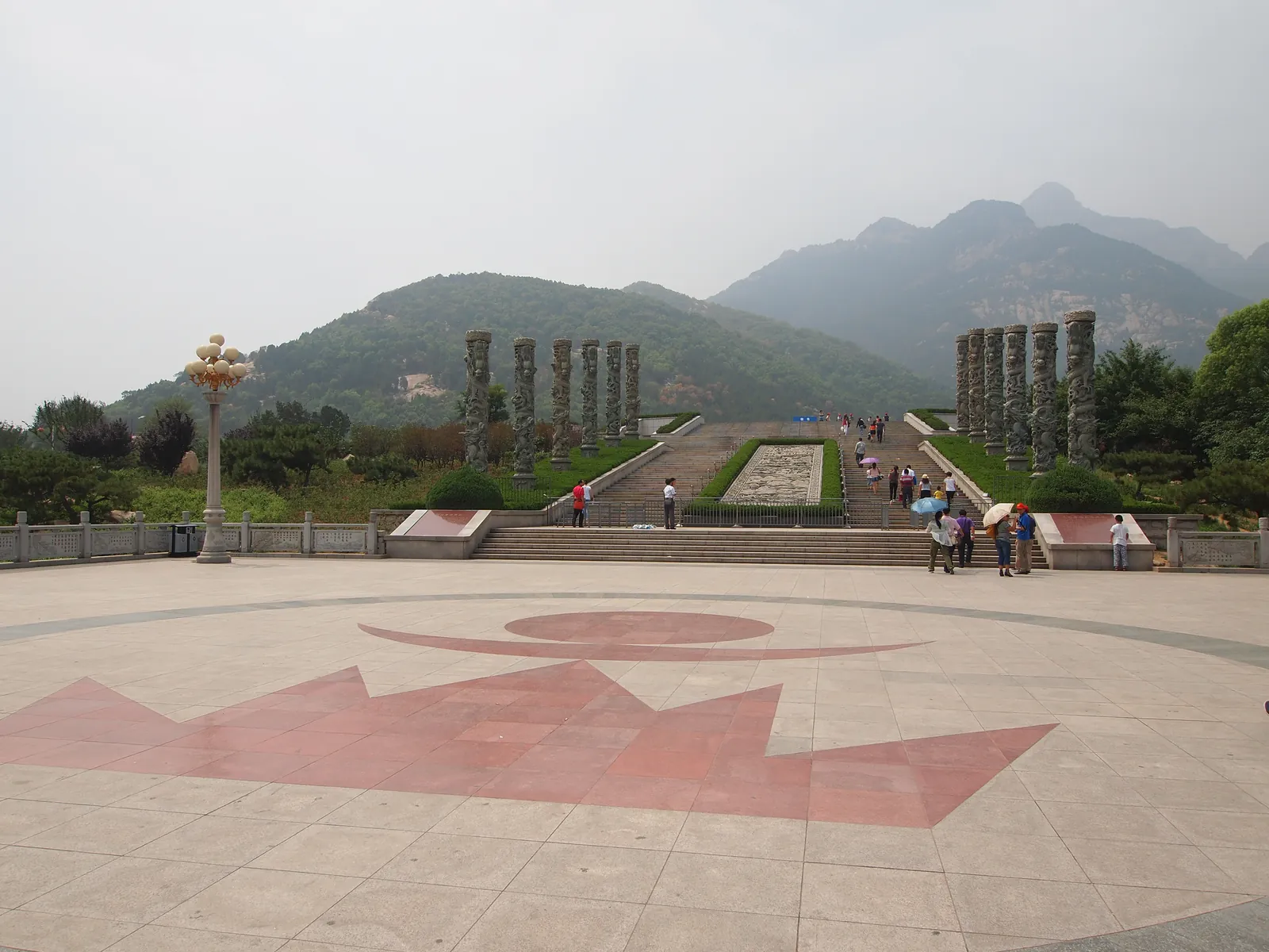 The paved plaza at Tianwaicun at the foot of Mount Tai, with stone columns, steps and the mountain ridge behind, where the shuttle bus to Zhongtianmen departs (Photo: rheins via Wikimedia Commons)