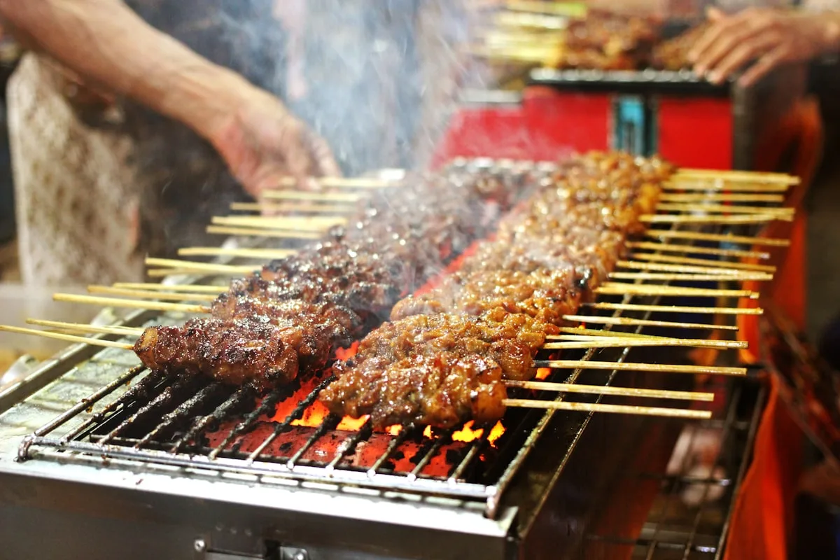 Des brochettes de viande grillant sur un brasero à charbon à un stand de nourriture de rue chinois, avec de la fumée qui monte