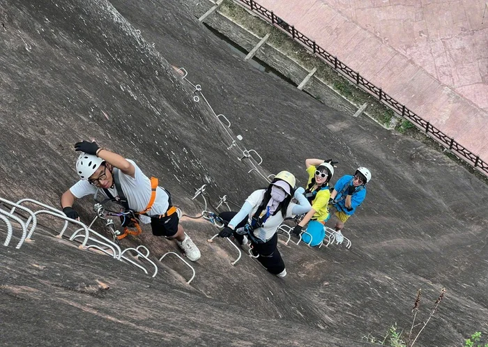 Four climbers in helmets and harnesses clipped to the safety cable on the via ferrata's rock slab