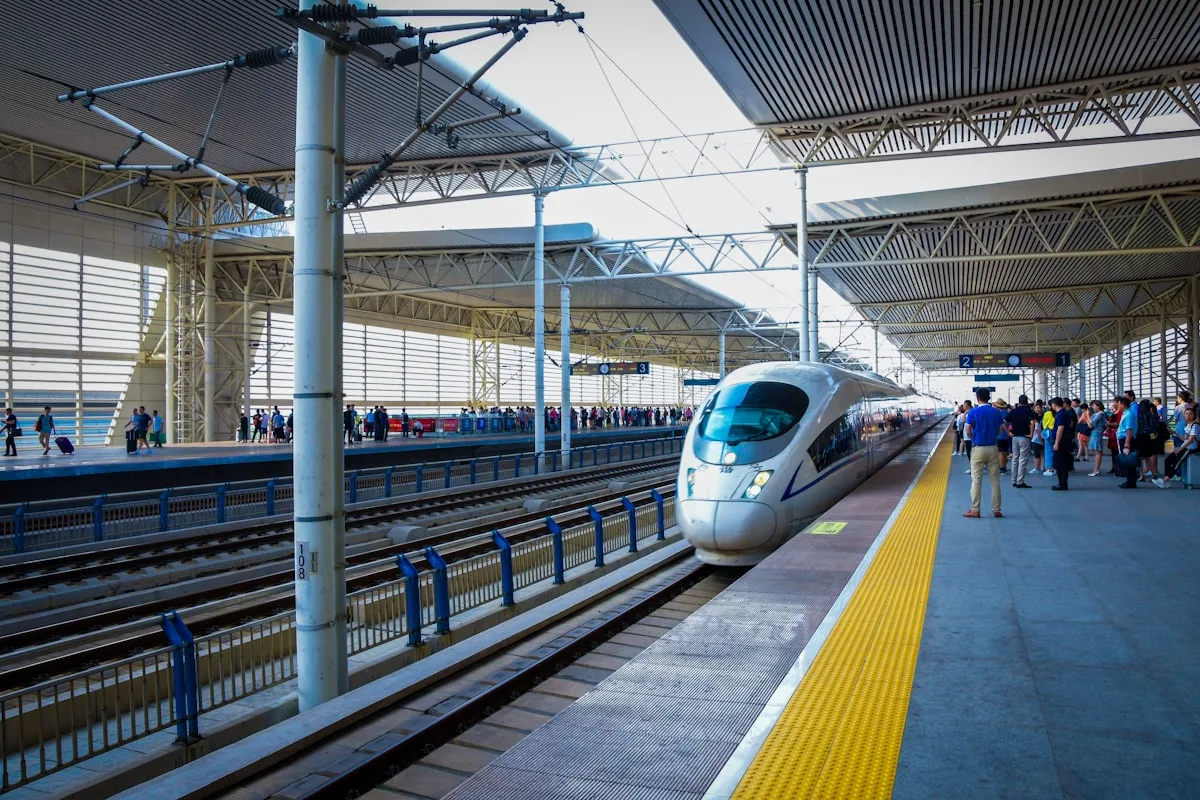 Un train à grande vitesse argenté à l'arrêt à un quai en Chine, des voyageurs attendant à côté