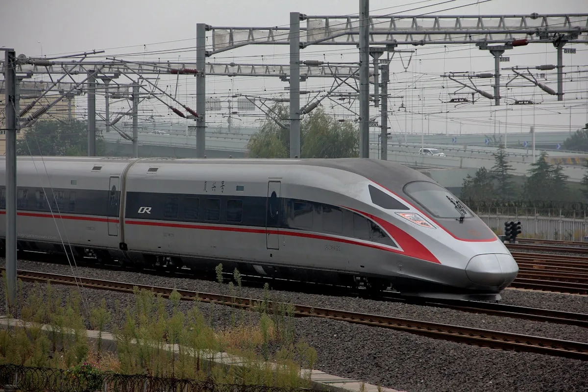 Un tren chino Fuxing de alta velocidad sobre su vía, con edificios de la ciudad y catenarias al fondo