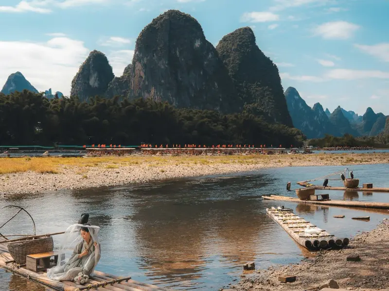 Sunset at Gongnong Bridge: bamboo rafts glide through golden light as karst peaks silhouette against the evening sky