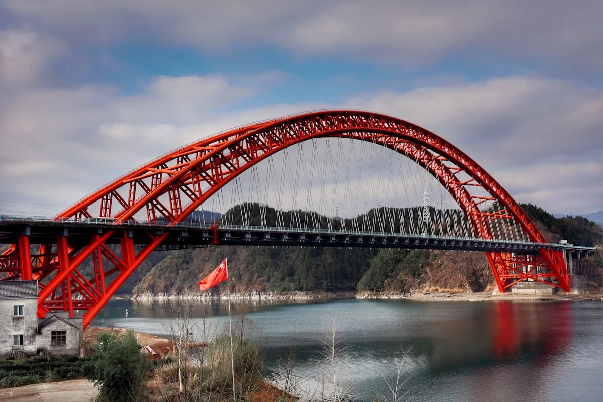 puente metálico rojo sobre río bajo cielo nublado durante el día