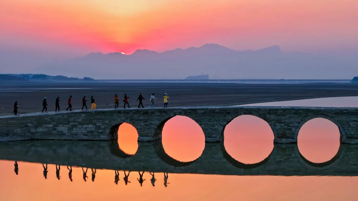 Gente camina por un puente con aberturas circulares al atardecer.
