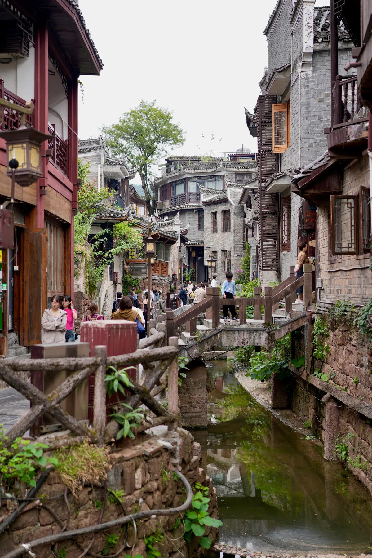 A stone lane in Fenghuang with a canal running between the old houses and visitors crossing a wooden footbridge (Photo: Lianguanlun via Wikimedia Commons)