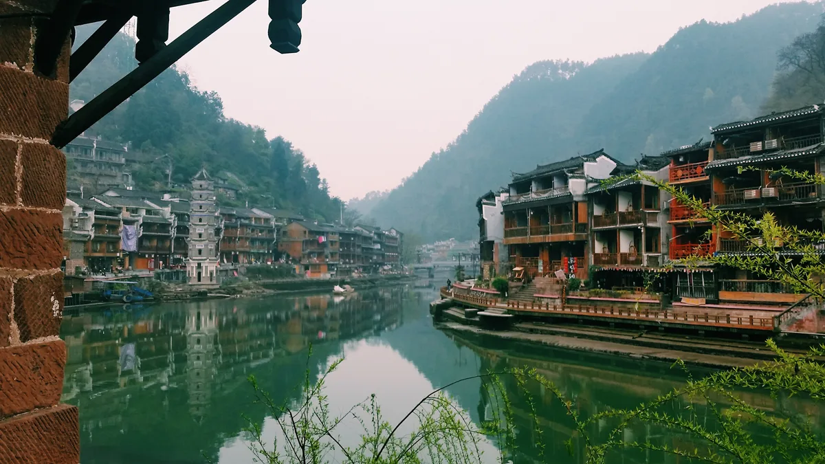 Morning haze over the Tuojiang at Fenghuang, with the town's roofs and a pagoda on the far bank reflected in the still water (Photo: Yunzhongjun via Wikimedia Commons)