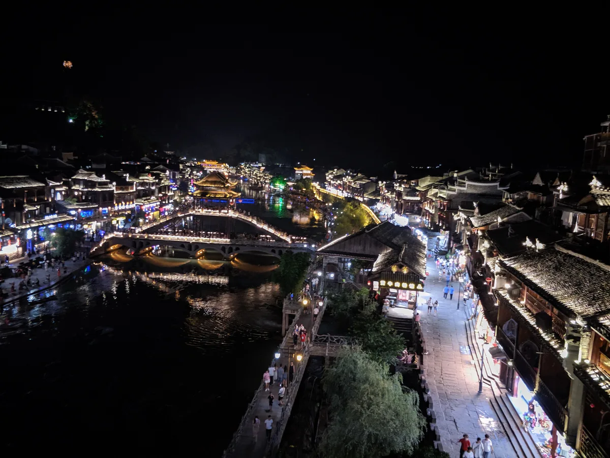 Fenghuang at night seen from above, with the lit Hongqiao bridge crossing the Tuojiang and crowds on the riverside walkways (Photo: Sunyiming via Wikimedia Commons)