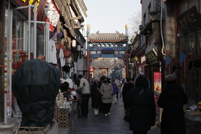 People walking down a narrow street lined with shops in Beijing's hutong neighborhood