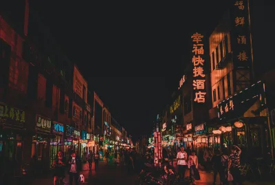 A busy Chinese commercial street at night, lit by shop signs in Chinese